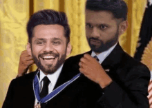 a man with a beard is wearing a medal around his neck while another man adjusts his tie .