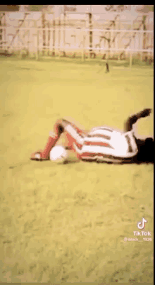 a soccer player is laying on the ground with a soccer ball in his hand .