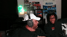 a man wearing headphones is sitting next to another man in front of a wii poster .