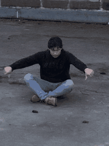 a man wearing a black sweatshirt that says ' dick ' on it sits on the ground with his arms outstretched