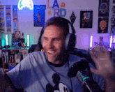 a man wearing headphones and a mickey mouse shirt is waving in front of a microphone