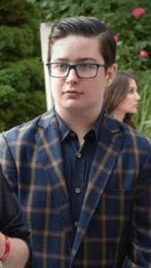 a young man wearing a plaid jacket and glasses is standing in front of a woman .