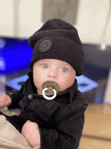 a baby with a pacifier in his mouth wearing a black converse hat