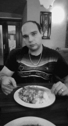 a man sitting at a table with a plate of food and a t-shirt that says executive protein