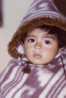 a young boy wearing a purple and white striped blanket with the letter g on it