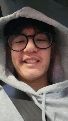 a man wearing glasses and a hoodie looks at the camera with his eyes closed