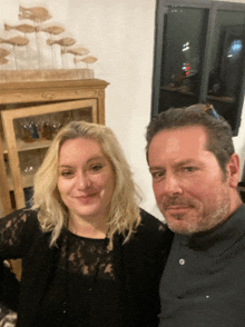 a man and a woman are posing for a picture in front of a glass cabinet