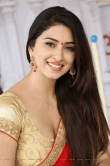 a woman wearing a gold blouse and a red saree smiles at the camera