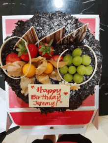 a birthday cake with strawberries grapes and a sign that says happy birthday jeremy