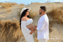 a man and a pregnant woman are standing on a sand dune and the name santos is on the bottom