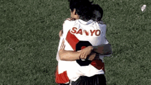 two soccer players hugging each other one of whom is wearing a sanyo jersey