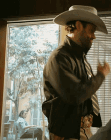 a man wearing a cowboy hat and tie stands in front of a window