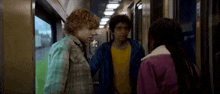 a group of young people are standing next to each other on a train talking to each other .