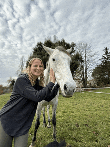 a woman is petting a white horse in a grassy field