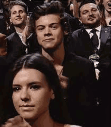 harry styles is sitting in a crowd of people watching a performance .