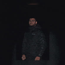 a man wearing a black columbia jacket stands in the dark