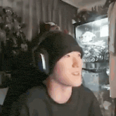 a man wearing headphones and a beanie is sitting in a chair in a room .