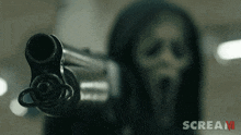 a person wearing a hooded mask is pointing a gun at the camera with the word scream in the corner