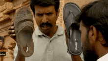 a man with a mustache is holding a pair of flip flops over his face .