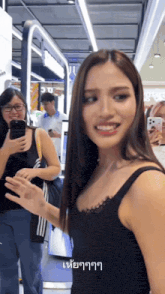 a woman in a black tank top is smiling in front of a group of people with their cell phones