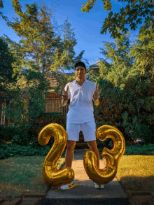 a man in a white shirt stands in front of a house with balloons that say 23