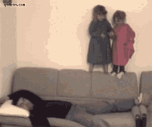 a man is sleeping on a couch while two little girls are standing on the couch