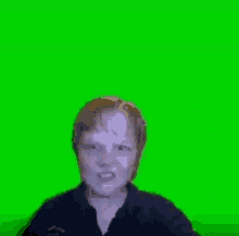 a young boy is standing in front of a green screen and making a funny face .