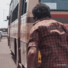 a man in a plaid shirt is standing in front of a bus that says sony music on it