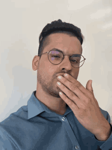 a man wearing glasses and a blue shirt covering his mouth with his hand