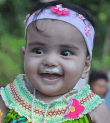 a baby girl wearing a headband and a pearl necklace is smiling .