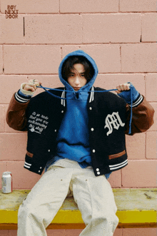 a man wearing a blue hoodie and a baseball jacket with the letter m on it