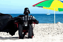 darth vader is sitting on the beach under an umbrella .