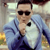 a man wearing sunglasses and a blue suit is pointing at the camera