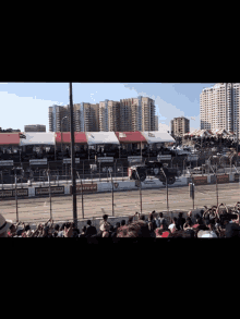 a crowd of people watching a race on a track that has a sign that says ' ford ' on it