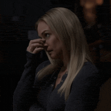 a woman in a black sweater holds her hand to her face
