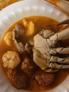 a crab is sitting in a bowl of sauce with shrimp and sausage