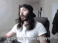 a man with long hair and a beard is sitting in a chair and saying woohoo yeah baby !
