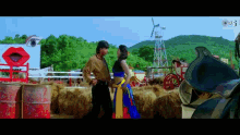 a man and a woman are standing next to each other in front of a hay bale in a field .