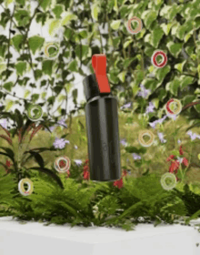 a black bottle with a red handle is surrounded by flowers