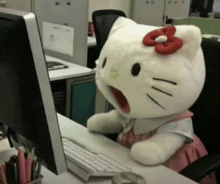 a stuffed hello kitty is sitting at a desk in front of a computer monitor