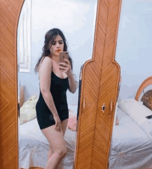 a woman in a black dress is taking a picture of herself in a mirror