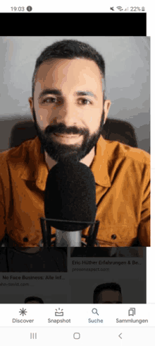 a man with a beard is speaking into a microphone on a phone screen