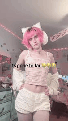 a girl with pink hair is standing in a room wearing a striped tank top and white shorts .