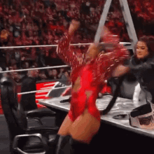 a woman in a red leotard is sitting in a chair in front of a crowd at a wrestling event .