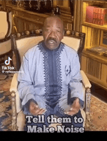 a man in a blue shirt is sitting in a chair and talking to someone .