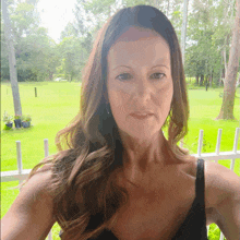 a woman in a black tank top is standing in front of a white fence