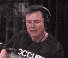 elon musk is wearing headphones and crying in front of a microphone .