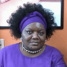 a woman with curly hair is wearing a purple headband and a necklace