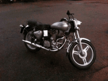 a silver royal enfield motorcycle is parked on a gravel road