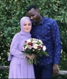 a man and a woman are posing for a picture with a bouquet of flowers .